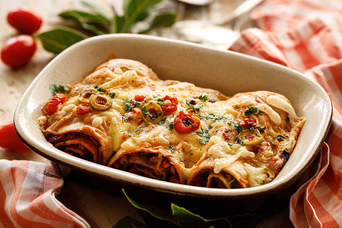 Baked vegetarian enchiladas stuffed with vegetables, sprinkled with cheese and herbs, served in a baking dish Baked vegetarian enchiladas stuffed with vegetables, sprinkled with cheese and herbs, served in a baking dish