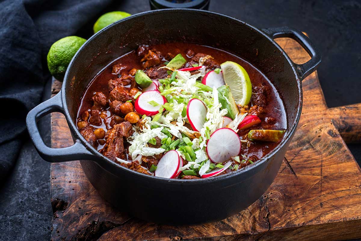 Traditional slow cooked Mexican pozole rojo as top view in a modern design cast-iron roasting dish on an old rustic wooden board Traditional slow cooked Mexican pozole rojo as top view in a modern design cast-iron roasting dish on an old rustic wooden board